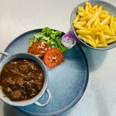 Bord met stoofvlees in bruine saus, een kommetje verse frieten, sla en tomaat