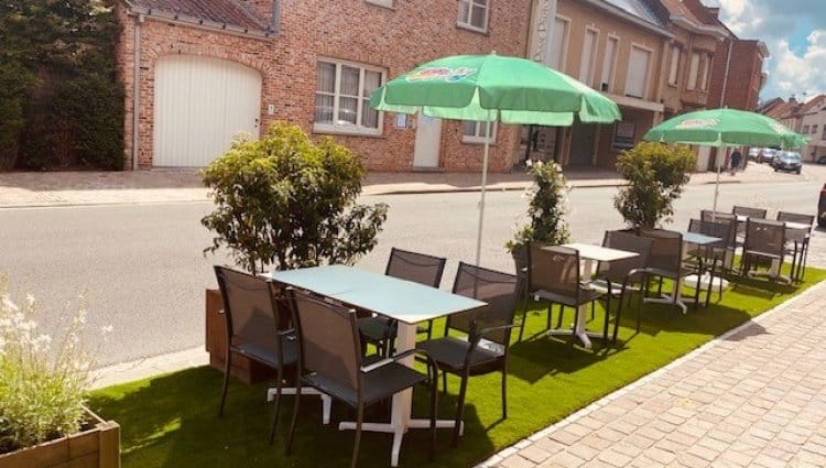 Het terras van Frituur Prinsenhof met groene parasols en tafels op kunstgras langs de straat